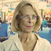 Older woman with blonde hair, glasses, and bright pink lipstick